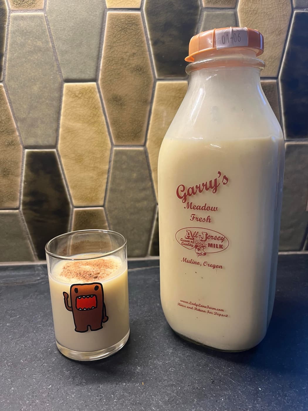 A bottle of fresh eggnog with a vintage label sits next to a glass filled with milk topped with a sprinkle of nutmeg