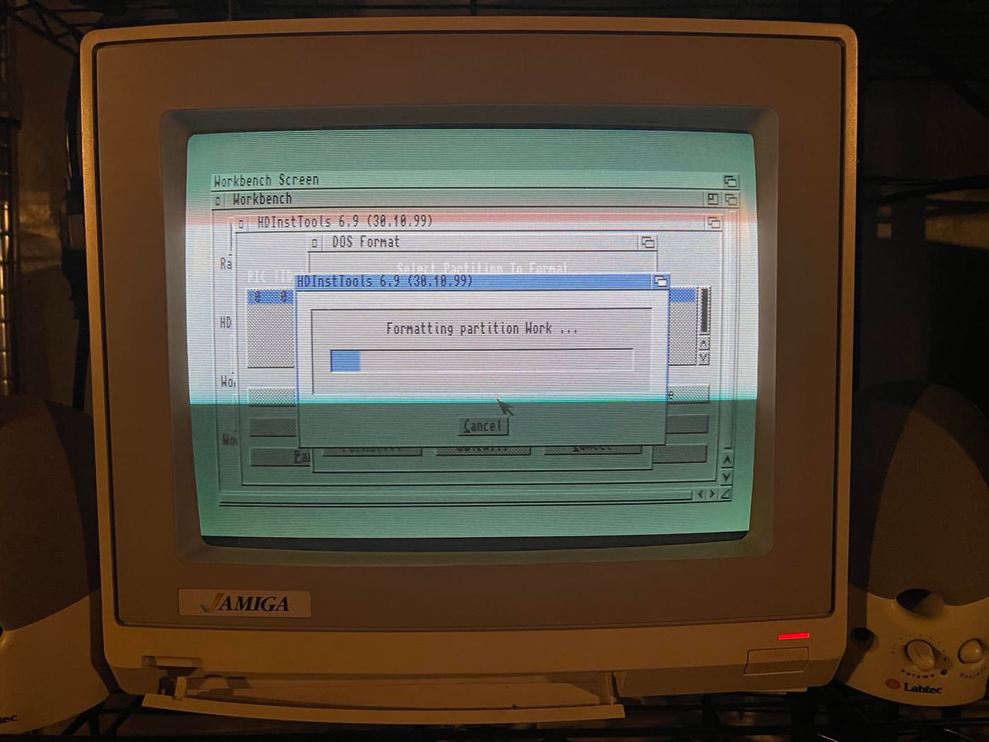 A vintage Amiga computer monitor displays the Workbench screen, showing a formatting process for a partition