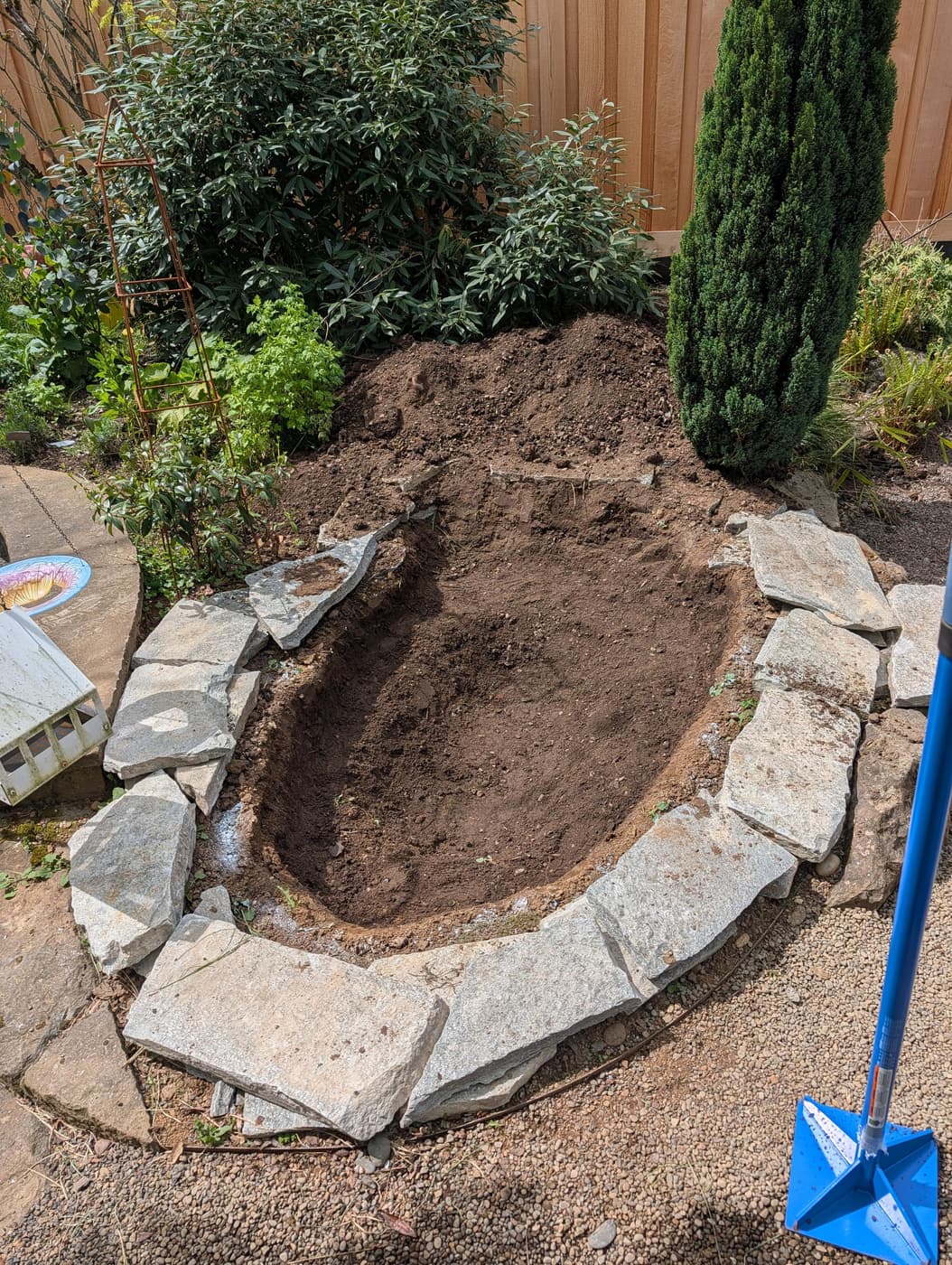 Photo of slate rocks surrounding a bathtub-sized hole dug in the dirt of a backyard