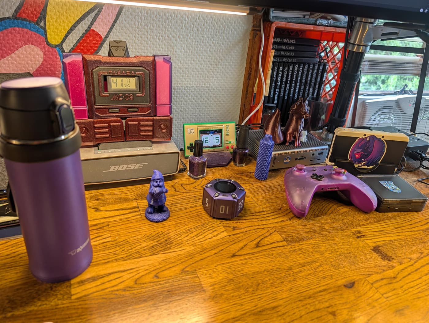 A cluttered wooden desk full of purple items: a game controller, a water bottle, and figurines