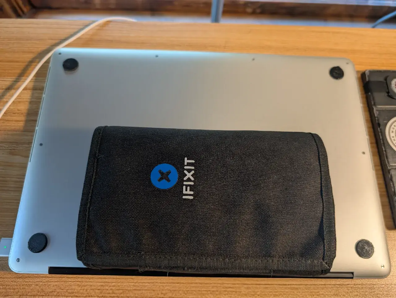 The closed MacBook Pro lying upside down on a desk with a black iFixit toolkit pouch resting on its underside
