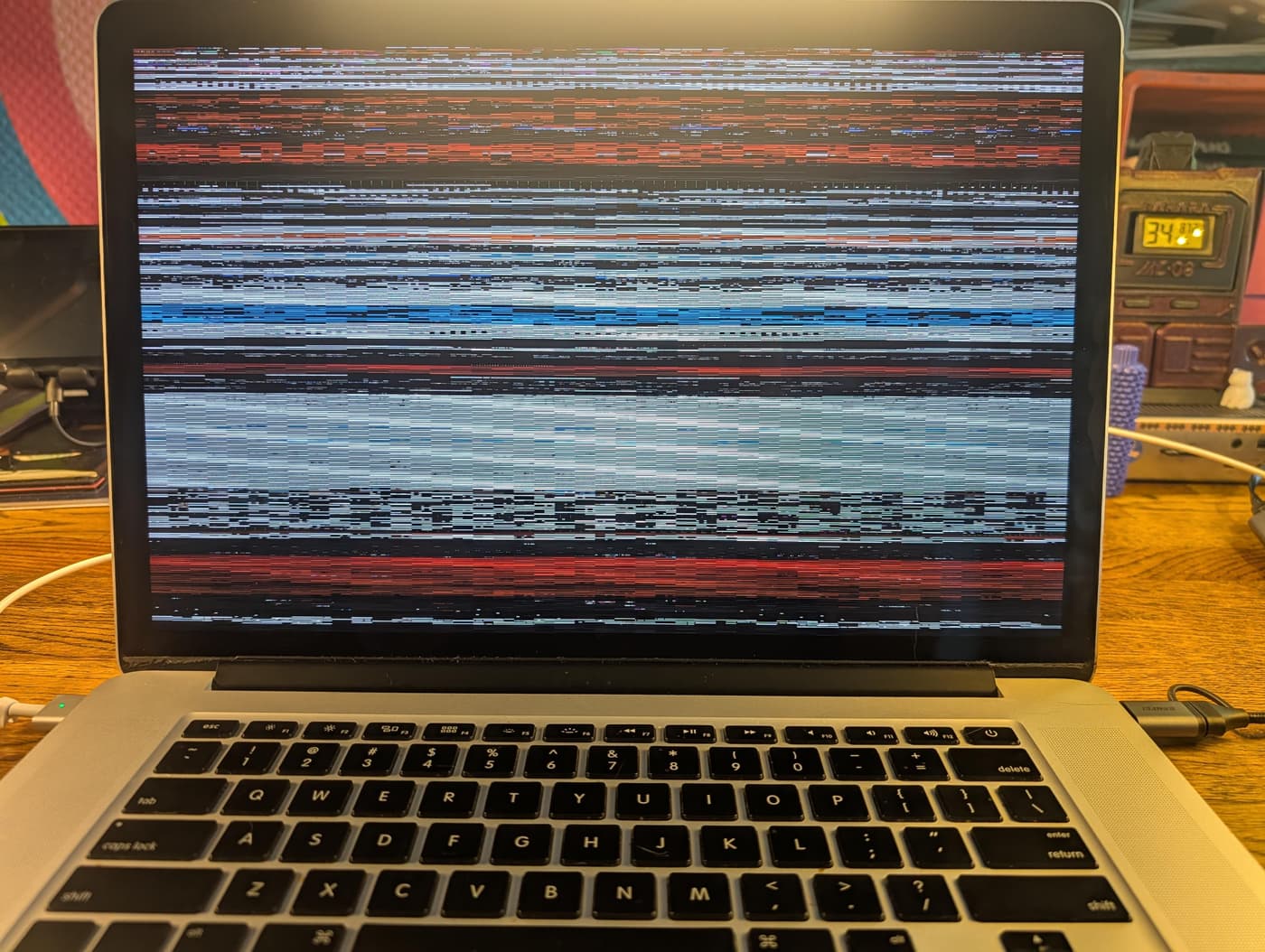 A silver MacBook Pro with its screen filled with colorful horizontal lines of static