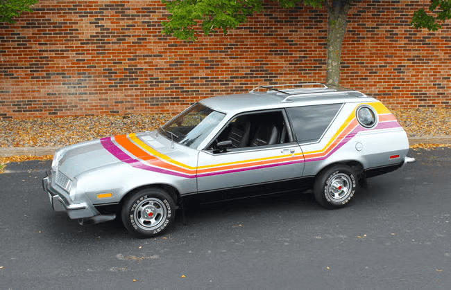A silver AMC Gremlin X, a 1970s hatchback with colorful orange, pink, and yellow stripes on its side.